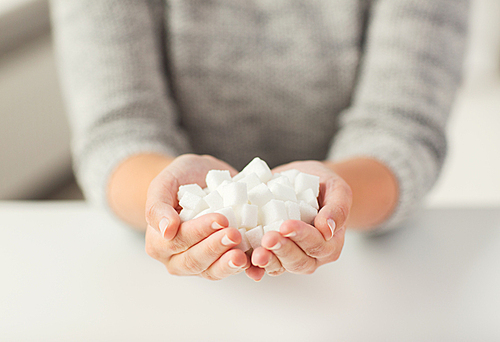 food, junk-food, diabetes and unhealthy eating concept - close up of white lump sugar in woman hands