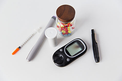 medicine, diabetes and health care concept - close up of glucometer, insulin pen, drug pills and other diabetic tools on table