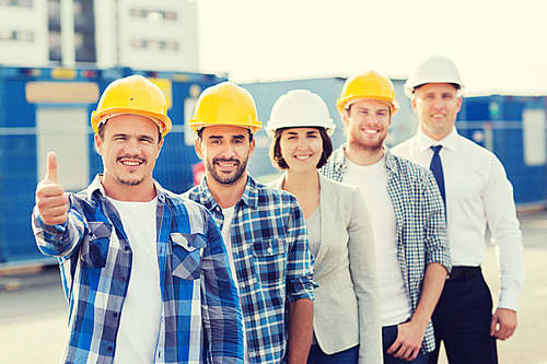 business, building, teamwork, gesture and people concept - group of smiling builders in hardhats showing thumbs up outdoors