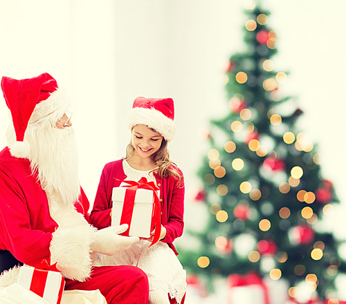 holidays, childhood and people concept - smiling little girl with santa claus and gifts over christmas tree lights lights background