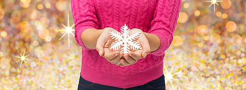 christmas, winter, holidays and people concept - close up of woman in pink sweater holding snowflake over golden lights background