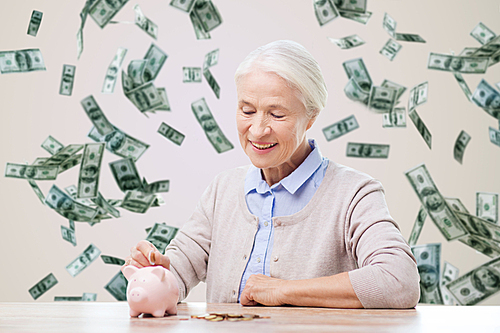 savings, finances, annuity insurance, retirement and people concept - smiling senior woman putting coins into piggy bank over money rain background