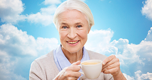 age, drink and people concept - happy smiling senior woman with cup of coffee over blue sky and clouds background