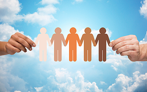 community, unity, population, race and humanity concept - multiracial couple hands holding chain of paper people pictogram over blue sky and clouds background