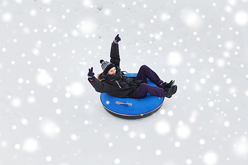 winter, leisure, sport, and people concept - happy teenage boy or young man sliding down on snow tube and showing victory gesture