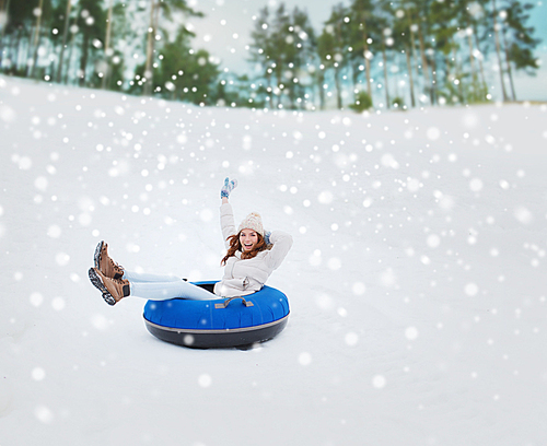 winter, leisure, sport, and people concept - happy teenage girl or woman sliding down on snow tube