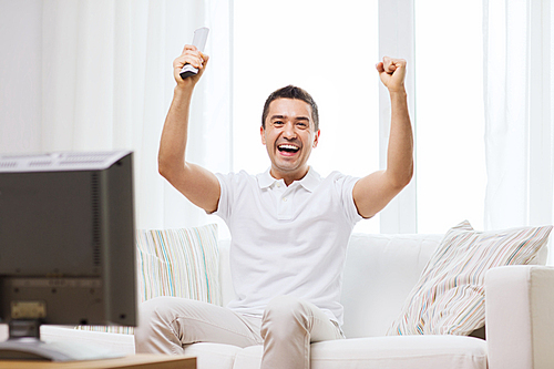 sports, happiness and people concept - smiling man watching sports on tv and supporting team at home