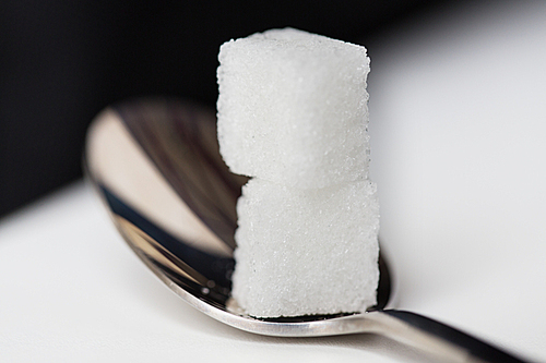 food, junk-food, diabetes and unhealthy eating concept - close up of white sugar cubes on teaspoon