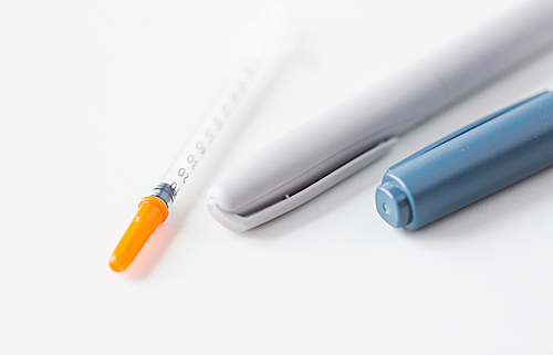 medicine, diabetes, medical tool and health care concept - close up of injection pen and disposable insulin syringe on table