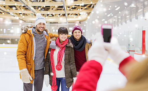 people, friendship, technology and leisure concept - happy friends taking photo with smartphone on skating rink