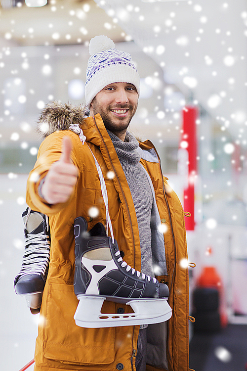 people, sport, gesture and leisure concept - happy young man with ice-skates showing thumbs up on skating rink
