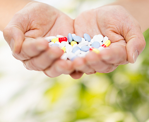 age, medicine, health care and people concept - close up of senior woman cupped hands with pills over green natural background