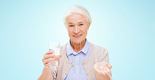 age, medicine, health care and people concept - happy senior woman with pills and glass of water over blue background