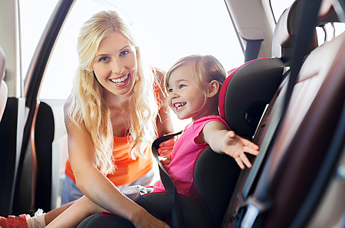family, transport, safety, road trip and people concept - happy mother fastening child with car seat belt