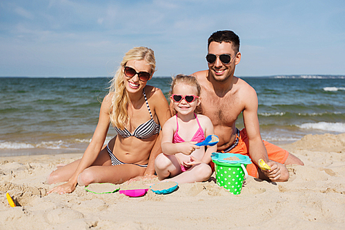 family, travel, vacation and people concept - happy man, woman and little girl in sunglasses playing with sand toys on summer beach