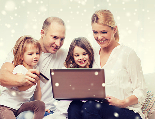 family, shopping, technology and people concept - happy family with laptop computer and credit card over snowflakes background