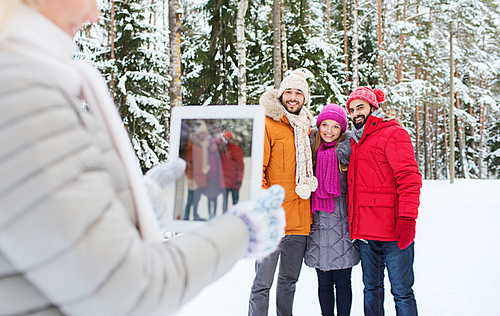 technology, season, friendship and people concept - group of smiling men and women taking picture with tablet pc computer in winter forest