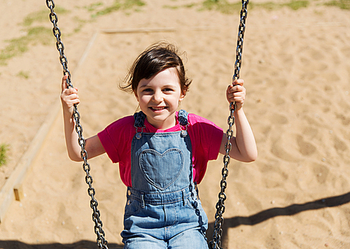 summer, childhood, leisure, friendship and people concept - happy little girl swinging on swing at children playground