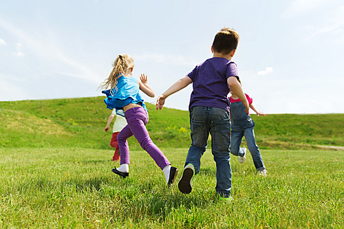 summer, childhood, leisure and people concept - group of happy kids playing tag game and running on green field outdoors