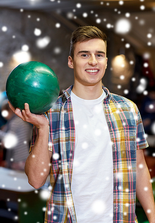 people, leisure, sport and entertainment concept - happy young man holding ball in bowling club at winter season