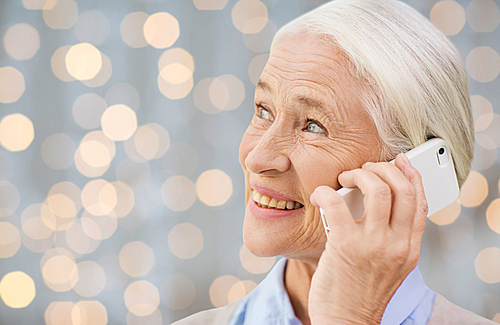 technology, communication age and people concept - happy senior woman with smartphone calling over holidays lights background