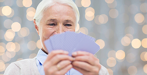 age, game, gamble, poker and people concept - close up of happy smiling senior woman playing cards over holidays lights background