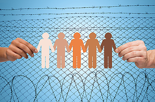 crime, imprisonment, refugee and humanity concept - multiracial couple hands holding chain of paper people pictogram over blue sky and barb wire background