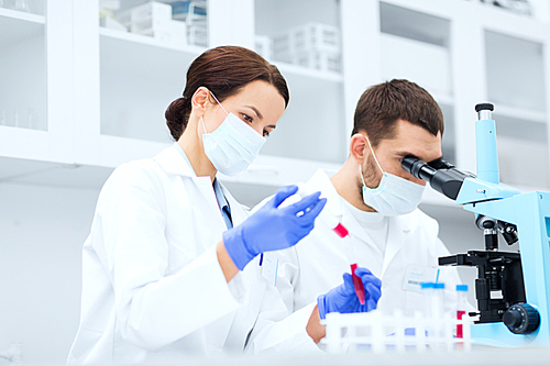 science, technology, biology and people concept - young scientists with pipette, test tube and microscope making research in clinical laboratory