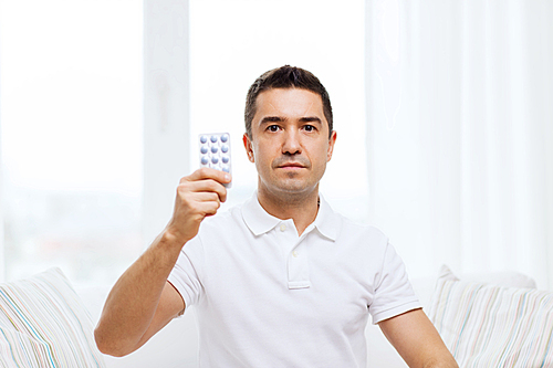 people, medication, medicine and health care concept - man showing pack of pills at home