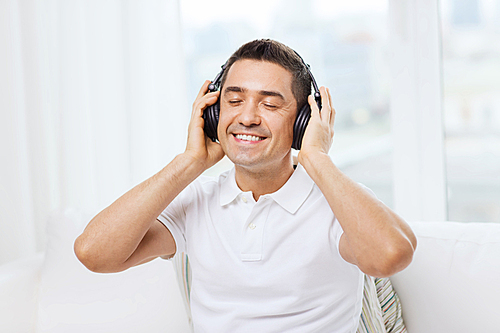 technology, people and lifestyle concept - happy man in headphones listening to music at home