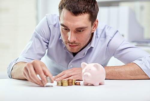 business, people, finances and money saving concept - businessman with piggy bank and coins at office