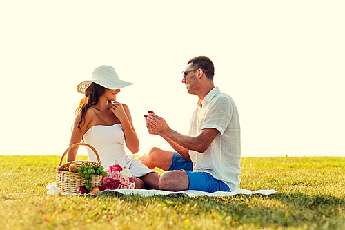 love, dating, people and holidays concept - smiling young man showing small red gift box to his girlfriend on picnic