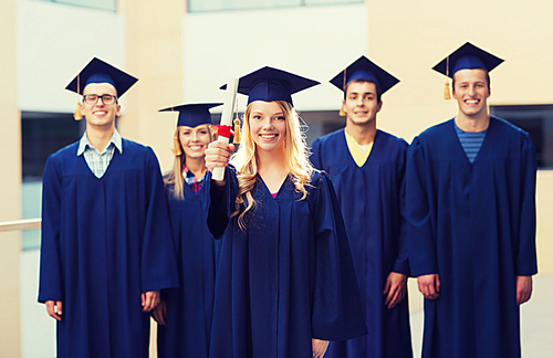 education, graduation and people concept - group of smiling students in mortarboards and gowns with diploma outdoors