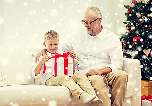 family, holidays, generation, christmas and people concept - smiling grandfather and grandson with gift box sitting on couch at home