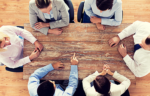 business, people and team work concept - close up of creative team sitting at table and pointing finger to something in office