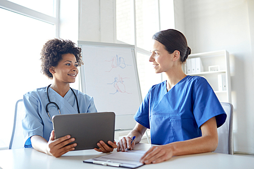 health care, people, technology and medicine concept -happy doctors with tablet pc computer and clipboard meeting and discussing something at hospital