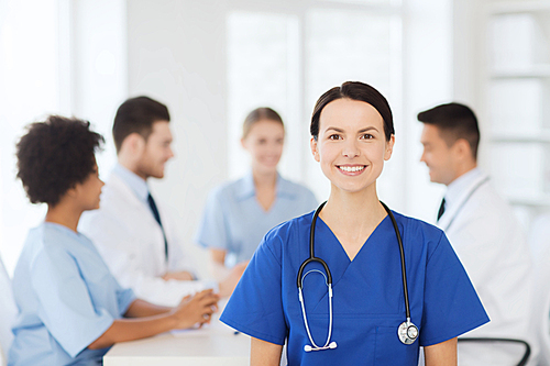 clinic, profession, people and medicine concept - happy female doctor over group of medics meeting at hospital