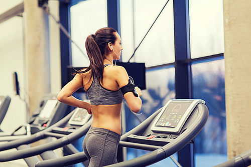 sport, fitness, lifestyle, technology and people concept - woman with smartphone or player and earphones exercising on treadmill in gym