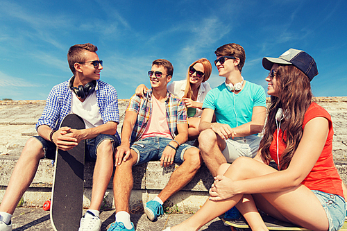 friendship, leisure, summer and people concept - group of smiling friends with skateboards sitting on city street