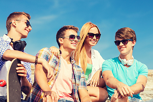 friendship, leisure, summer and people concept - group of smiling friends with skateboard sitting on city street