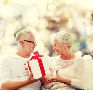 family, holidays, christmas, age and people concept - happy senior couple with gift box over lights background