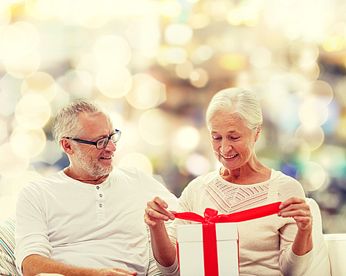 family, holidays, christmas, age and people concept - happy senior couple with gift box over lights background