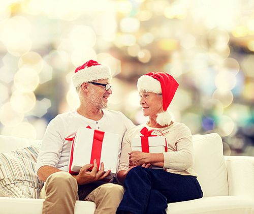 family, holidays, christmas, age and people concept - happy senior couple in santa helper hats with gift boxes over lights background