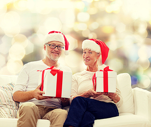 family, holidays, christmas, age and people concept - happy senior couple in santa helper hats with gift boxes over lights background