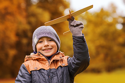 autumn, childhood, dream, leisure and people concept - happy little boy playing with wooden toy plane outdoors