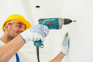 building, working equipment and people concept - close up of happy builder in hardhat perforating wall with drill indoors