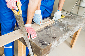 building, carpentry, repair, teamwork and people concept - close up of builders with arm saw sawing board on table