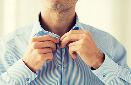 people, business, fashion and clothing concept - close up of man dressing up and fastening buttons on shirt at home