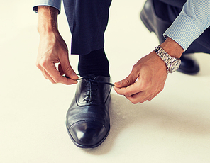 people, business, fashion and footwear concept - close up of man leg and hands tying shoe laces