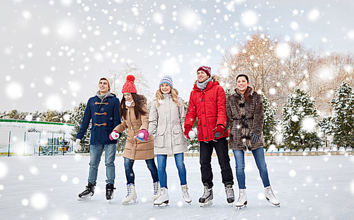 people, winter, friendship, sport and leisure concept - happy friends ice skating on rink outdoors